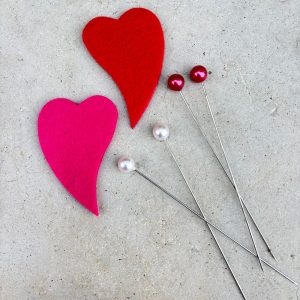 Punainen ja pinkki huopasydän ja kaksi neulaa helmänvärisellä ja punaisessa päällä
